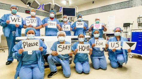 A group of nurses in scrubs, each holding a sign- together reading "We stay here for you, please stay home for us!"